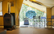 Vista dall'interno della tenda safari Bungalow Trappeur poêle a Huttopia Lac de Sillé, con stufa e terrazza.