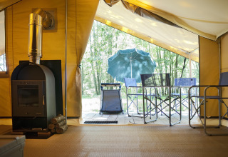 Blik uit de safaritent Bungalow Trappeur poêle bij Huttopia Lac de Sillé met houtkachel en terrasstoelen.
