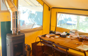 Indvendigt billede af en safari telt med brændeovn og træbord, Bungalow tent Trappeur poêle, Huttopia Lac de Sillé.