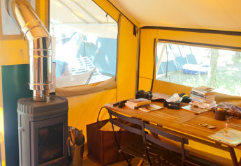 Interior of a safari tent with wood stove and table, Bungalow tent Trappeur poêle at Huttopia Lac de Sillé, France.