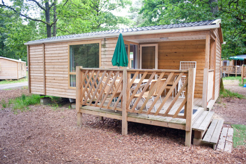 Houten mobiel huisje Cottage met veranda en buitentafel, omgeven door groene bomen en natuur.