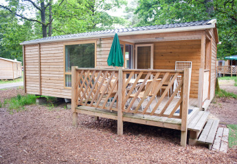 Casa móvil Cottage de madera con porche y mesa exterior, rodeada de árboles verdes y naturaleza.