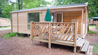Wooden mobile home Cottage with a covered porch, outdoor dining set, and surrounded by leafy trees.