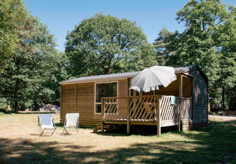 Stacaravan Cottage bij Huttopia Lac de Sillé in Frankrijk met veranda, parasol en boszicht.