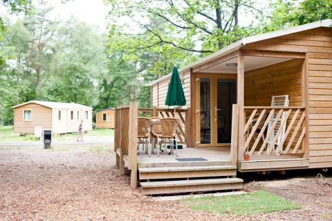Stacaravan Cottage bij Huttopia Lac de Sillé in Frankrijk met houten terras en groene bosrijke omgeving.