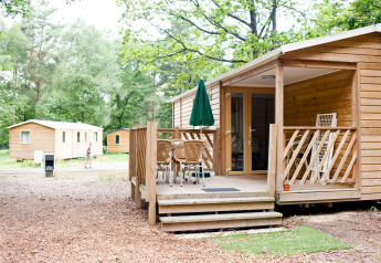 Stacaravan Cottage bij Huttopia Lac de Sillé in Frankrijk met houten terras en groene bosrijke omgeving.