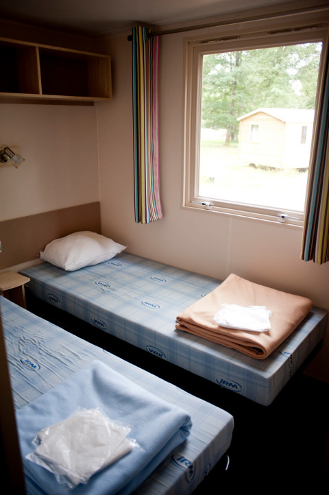 To enkeltsenge i et mobilhome Cottage på Huttopia Lac de Sillé i Frankrig med vindue og udsigt.