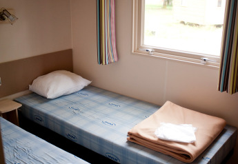 Zwei Einzelbetten im Mobile Home Cottage bei Huttopia Lac de Sillé in Frankreich mit Fensterblick.