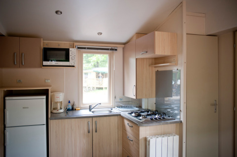Compacte keuken in een Mobile home Cottage bij Huttopia Lac de Sillé, Frankrijk, met apparaten en raam.