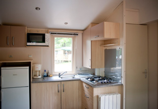 Compacte keuken in een Mobile home Cottage bij Huttopia Lac de Sillé, Frankrijk, met apparaten en raam.