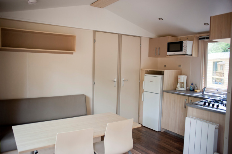 Interior view of Mobile home Cottage at Huttopia Lac de Sillé, France, showing a compact kitchen and table.