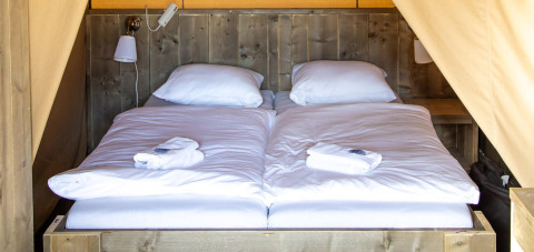 Interior acogedor con dos camas individuales juntas y ropa de cama blanca en una tienda safari Base Lodge.