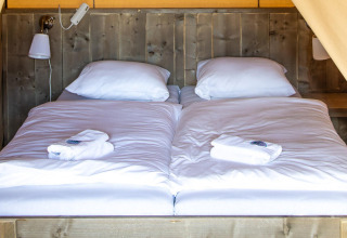 Interior acogedor con dos camas individuales juntas y ropa de cama blanca en una tienda safari Base Lodge.