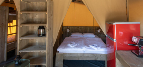 Interior de la tienda safari Base Lodge con cama doble, nevera roja y estantes de madera en Croacia.