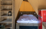 Interior de la tienda safari Base Lodge con cama doble, nevera roja y estantes de madera en Croacia.
