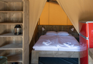 Interior de la tienda safari Base Lodge con cama doble, nevera roja y estantes de madera en Croacia.