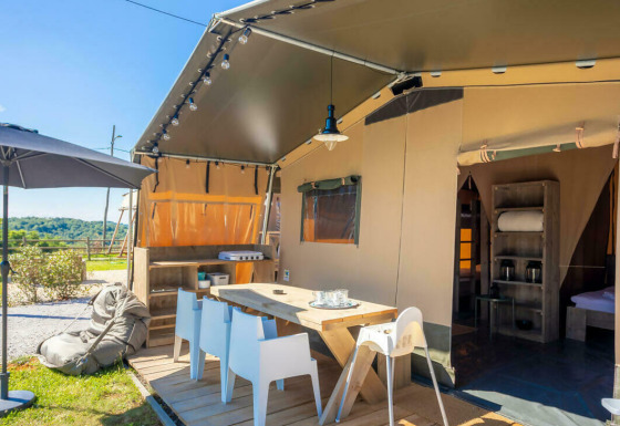 Zona exterior en la tienda safari Base Lodge con terraza, mesa de comedor, sombrilla y vistas al campo.