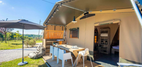 Außenbereich des Safari-Zeltes Base Lodge mit Terrasse, Esstisch, Sonnenschirm und Naturblick.