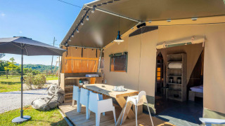Zona exterior en la tienda safari Base Lodge con terraza, mesa de comedor, sombrilla y vistas al campo.