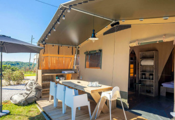 Zona exterior en la tienda safari Base Lodge con terraza, mesa de comedor, sombrilla y vistas al campo.