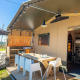 Zona exterior en la tienda safari Base Lodge con terraza, mesa de comedor, sombrilla y vistas al campo.