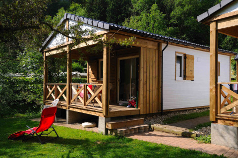Moderne glampinghut met houten terras en rode ligstoel, gelegen in een groene omgeving van een vakantiepark.