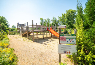 Legeplads i solskin ved Camping Les 3 Cantons, Occitanie, Frankrig, omgivet af grønne træer og blomster.
