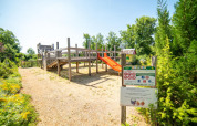 Legeplads i solskin ved Camping Les 3 Cantons, Occitanie, Frankrig, omgivet af grønne træer og blomster.