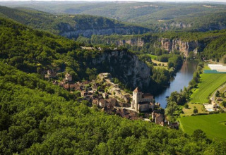 Aerial view of Camping Les 3 Cantons holiday park in Occitanie, France, surrounded by lush forest and river.