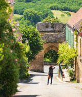 Una persona camina por una pintoresca calle rodeada de casas de piedra en Saint-Antonin-Noble-Val, Occitanie, Francia.