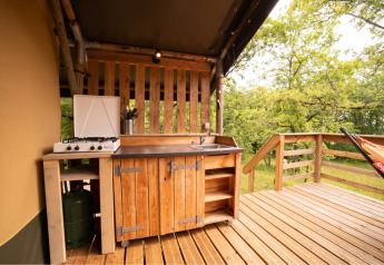 Buitenkeuken op het terras van een safaritent met gasvuur, houten kasten, spoelbak en zicht op het bos.