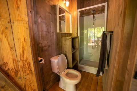 Bagno in una tenda safari con toilette, box doccia, pareti in legno e asciugamani su un supporto.