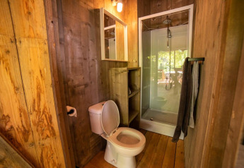 Bathroom in a safari tent featuring a toilet, shower stall, wooden walls, and towels on a rack.