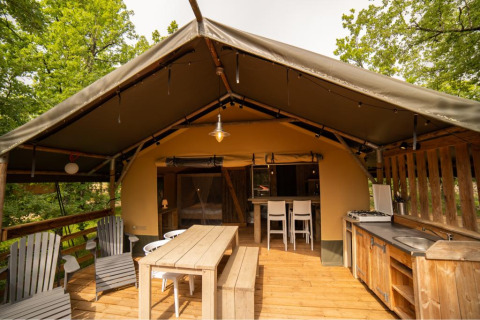 Safaritent met houten meubilair, buitenkeuken en zithoek op een overdekt terras tussen de bomen.