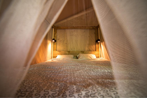 Knusse binnenaanzicht van een bed met patronen beddengoed en lampjes in een houten safaritent.