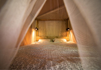 Knusse binnenaanzicht van een bed met patronen beddengoed en lampjes in een houten safaritent.