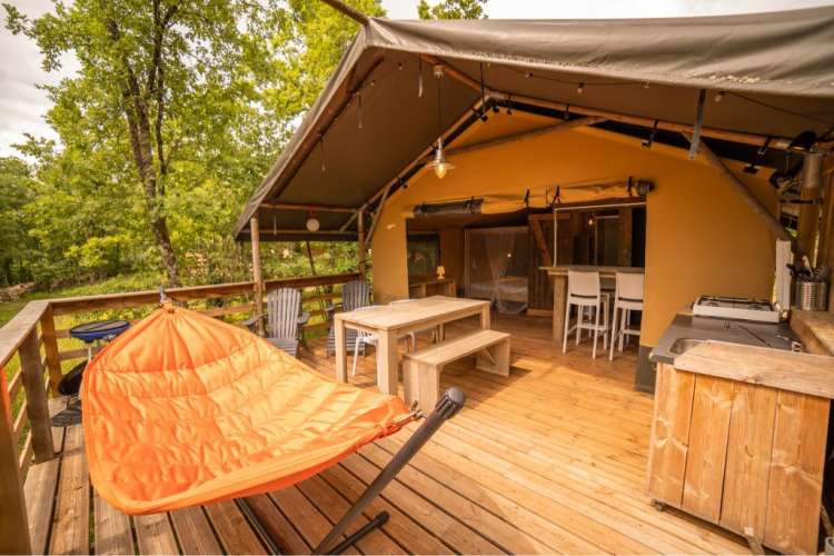 Holzterrasse eines Safarizelts mit Sitzgarnitur, Hängesessel und Blick ins Grüne.