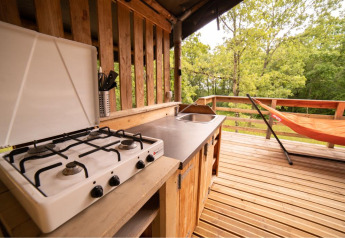 Buitenkeuken met gasvuur, spoelbak en oranje hangmat op houten terras naast een safaritent.