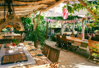 Buiten eetgedeelte bij Camping Les 3 Cantons in Occitanië, Frankrijk, met houten tafels en groene planten.