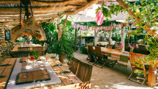 Zona de comedor al aire libre en Camping Les 3 Cantons, Occitanie, Francia, con mesas rústicas y plantas.