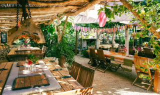 Zona de comedor al aire libre en Camping Les 3 Cantons, Occitanie, Francia, con mesas rústicas y plantas.