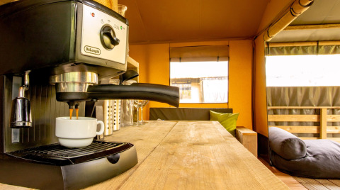 Espressomachine op houten tafel in de safaritent Wood Lodge op Camping Les 3 Cantons, Frankrijk, gezellig interieur.