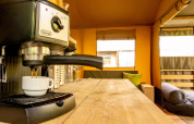 Cafetera espresso en mesa de madera dentro de tienda safari Wood Lodge en Camping Les 3 Cantons, Francia.