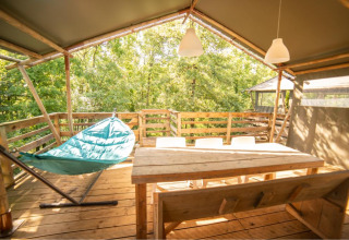 Terrazza in legno soleggiata con amaca, tavolo e sedie al safari tent Wood Lodge, Camping Les 3 Cantons, Francia
