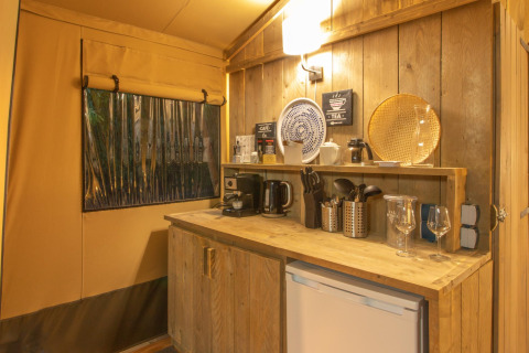 Keukenhoek in de safari tent Wood Lodge bij Camping Les 3 Cantons in Frankrijk, met houten meubels en servies.
