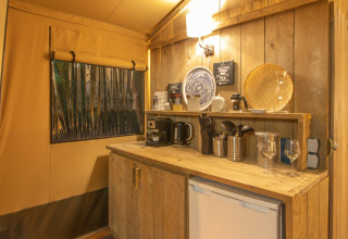 Rincón de cocina en tienda safari Wood Lodge en Camping Les 3 Cantons, Francia, con muebles de madera y utensilios.