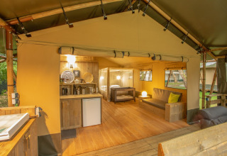 Vista interior de una tienda safari Wood Lodge en Camping Les 3 Cantons, Francia, con muebles de madera.