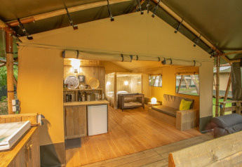 Vista interior de una tienda safari Wood Lodge en Camping Les 3 Cantons, Francia, con muebles de madera.