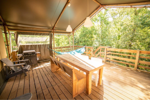 Holzterrasse mit Esstisch, Hängematte, Grill und Blick auf den Wald an einem Wood Lodge Safari-Zelt in Frankreich.