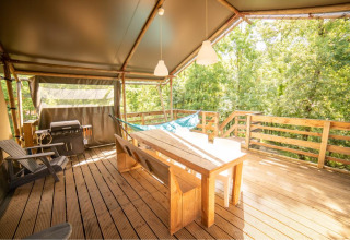 Terraza de madera con mesa de comedor, hamaca, parrilla y vista al bosque en una tienda safari Wood Lodge en Francia.